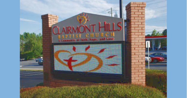 Clairmont Hills Baptist Church sign: red text, digital display, heart & cross graphic, brick pillars, on a sunny day.