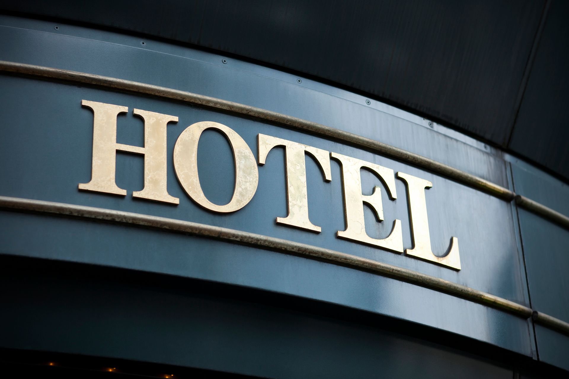 Gold “HOTEL” sign mounted on dark background, marking entrance of building exterior. Gold “HOTEL” sign mounted on dark background, marking entrance of building exterior.