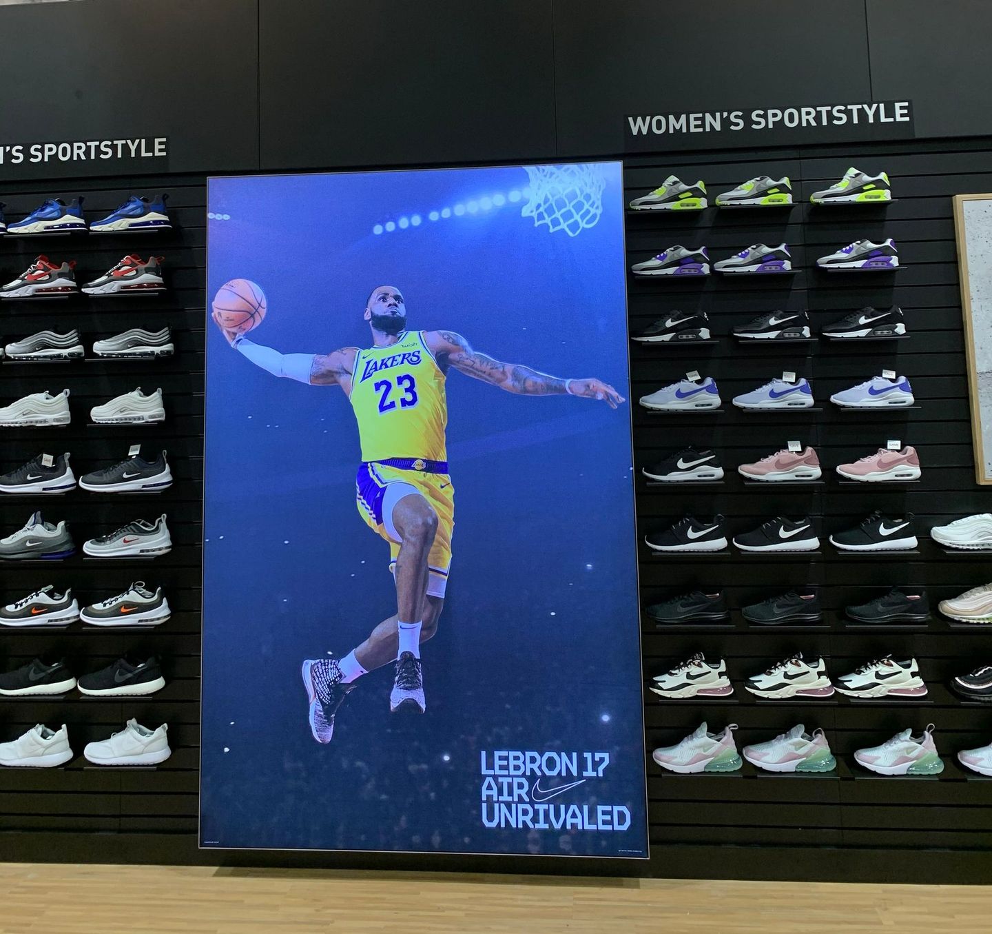 LeBron James poster in a shoe store. He wears a Lakers jersey and holds a basketball, surrounded by shoes.