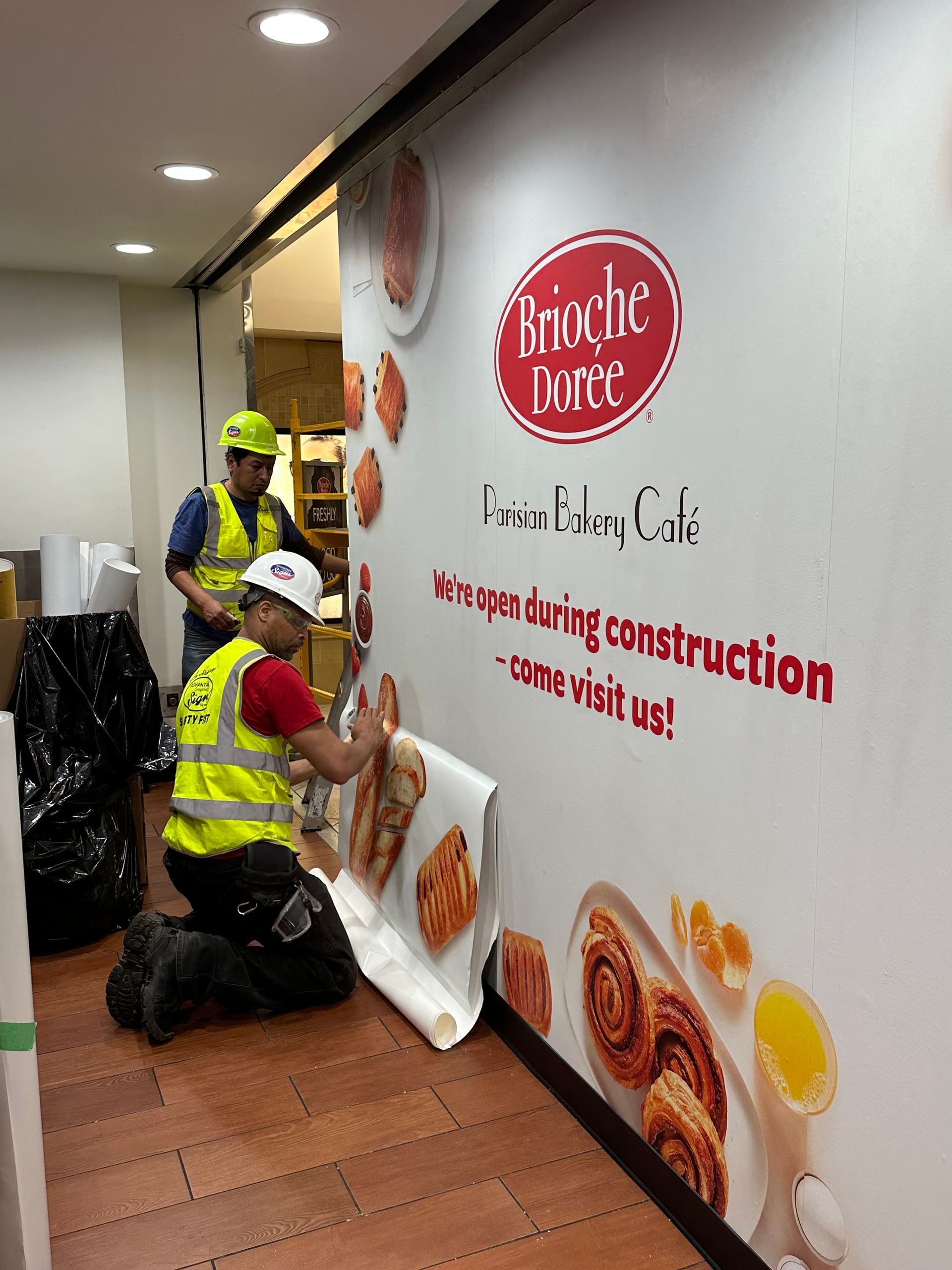A man is kneeling down in front of a sign that says ' brioche dorée ' on it.