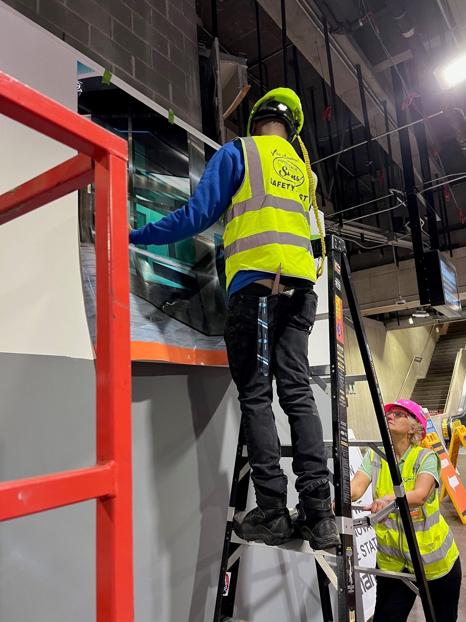 A man in a yellow vest is standing on a ladder.