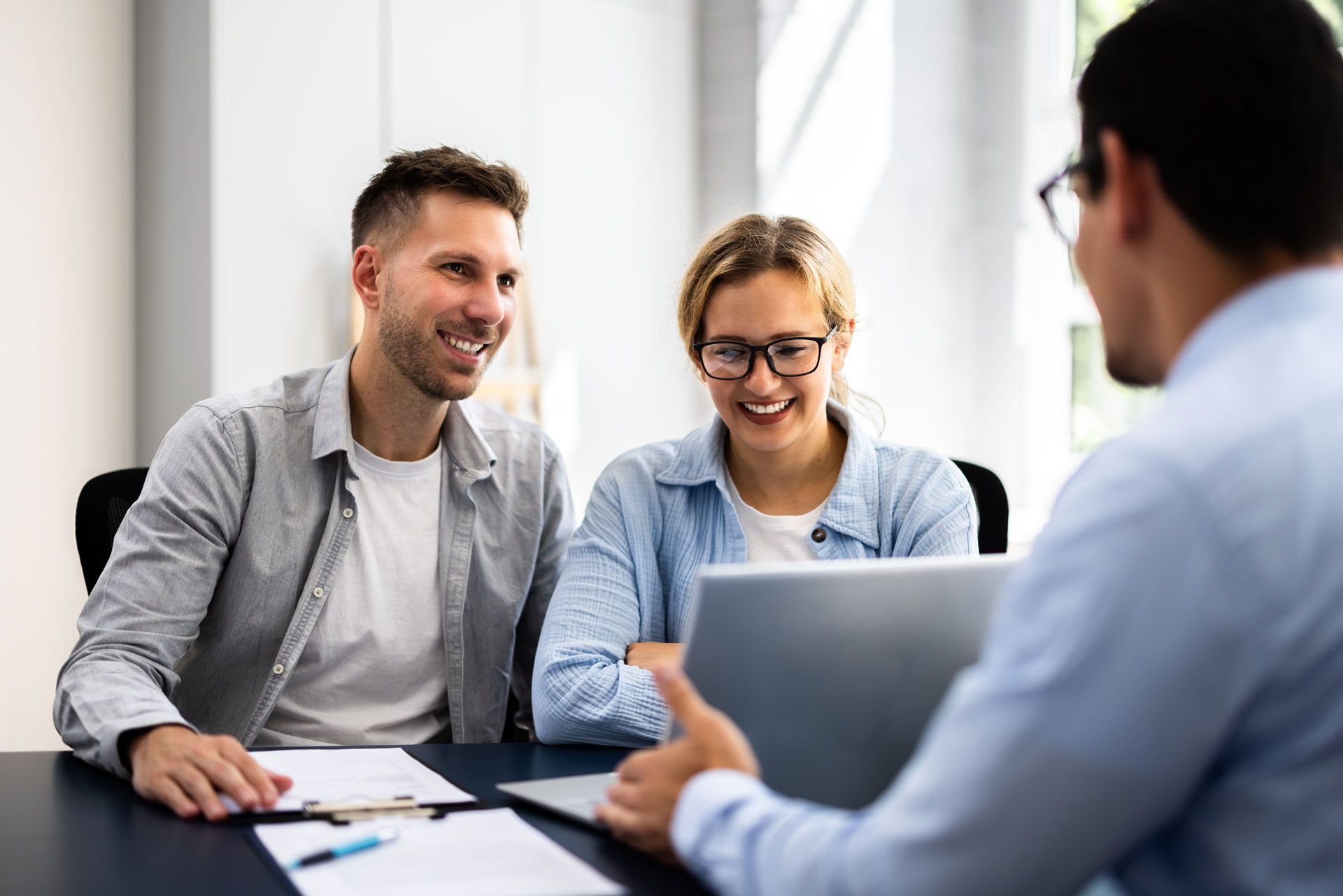 Two people smiling during a laptop meeting with a third person in an office setting