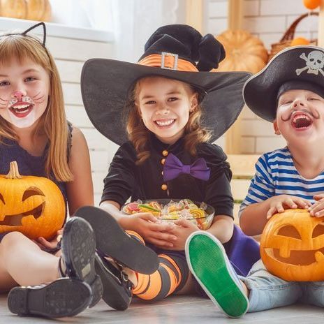 Three children dressed for Halloween with carved pumkins. 