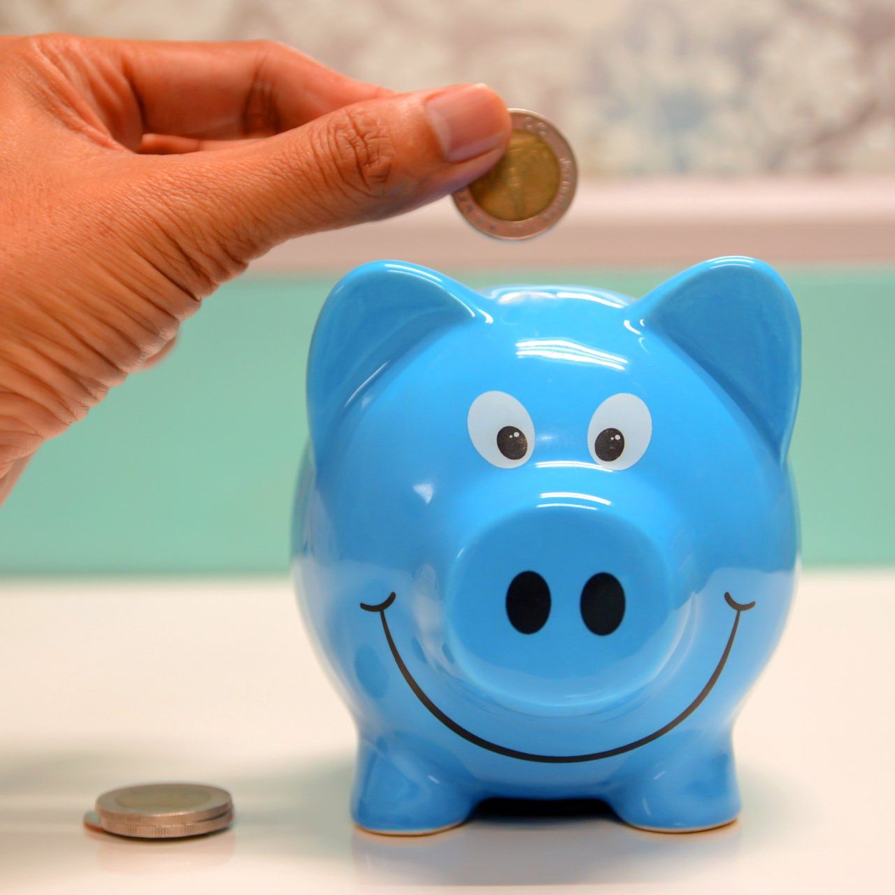 Hand putting coin into a blue piggy bank.