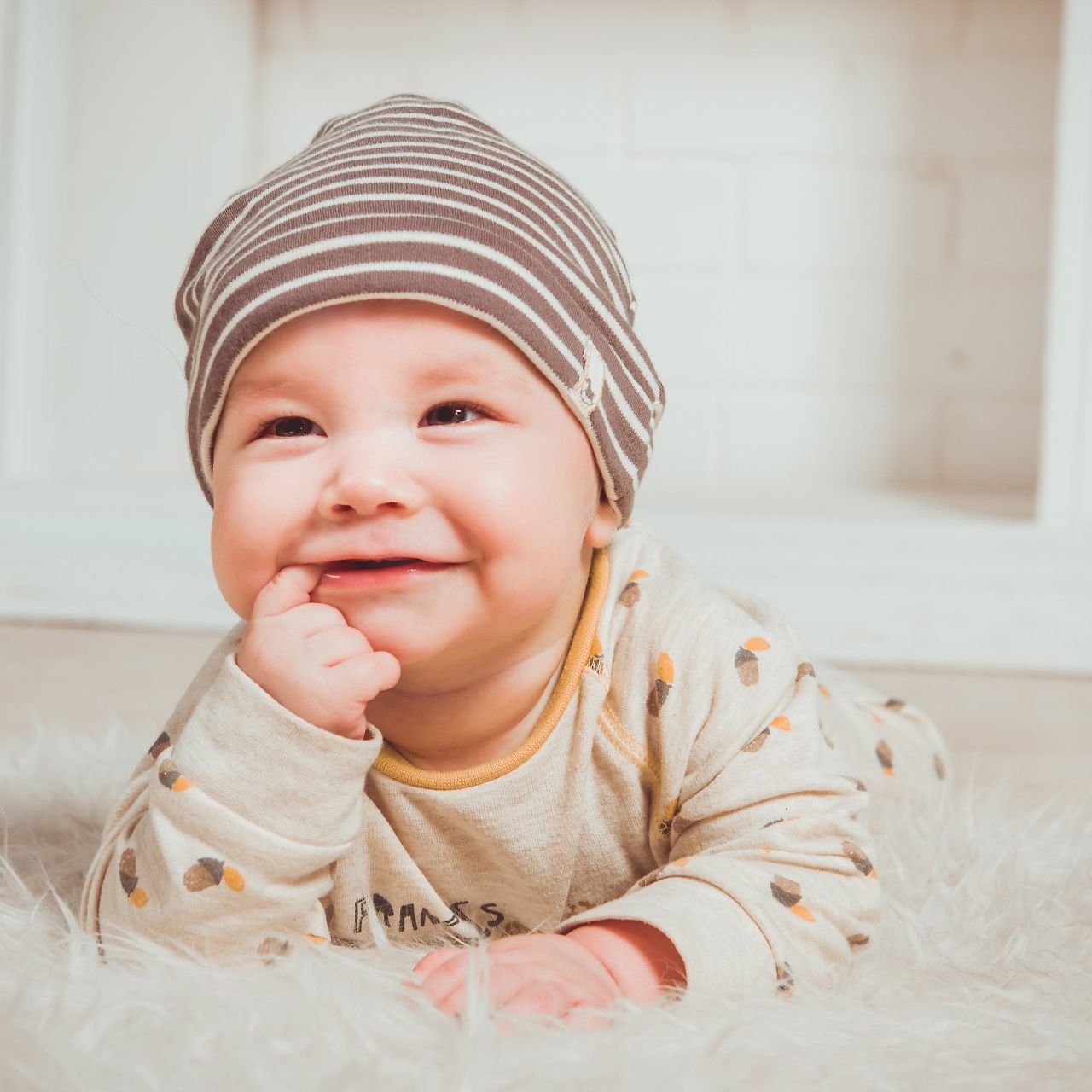 Image of infant with finger in mouth smiling.