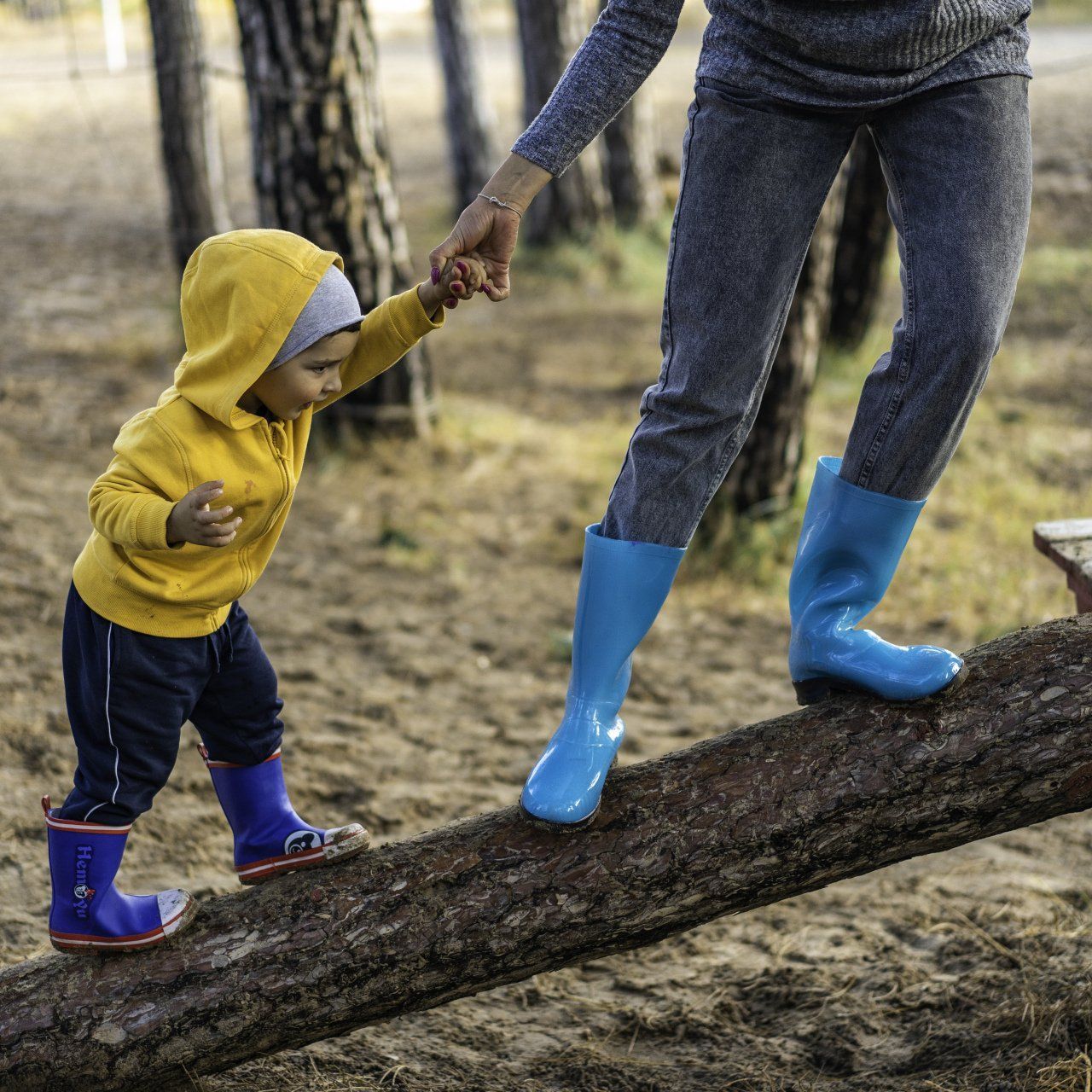 Image of parent helping toddler climb up a fallen tree enjoying nature.