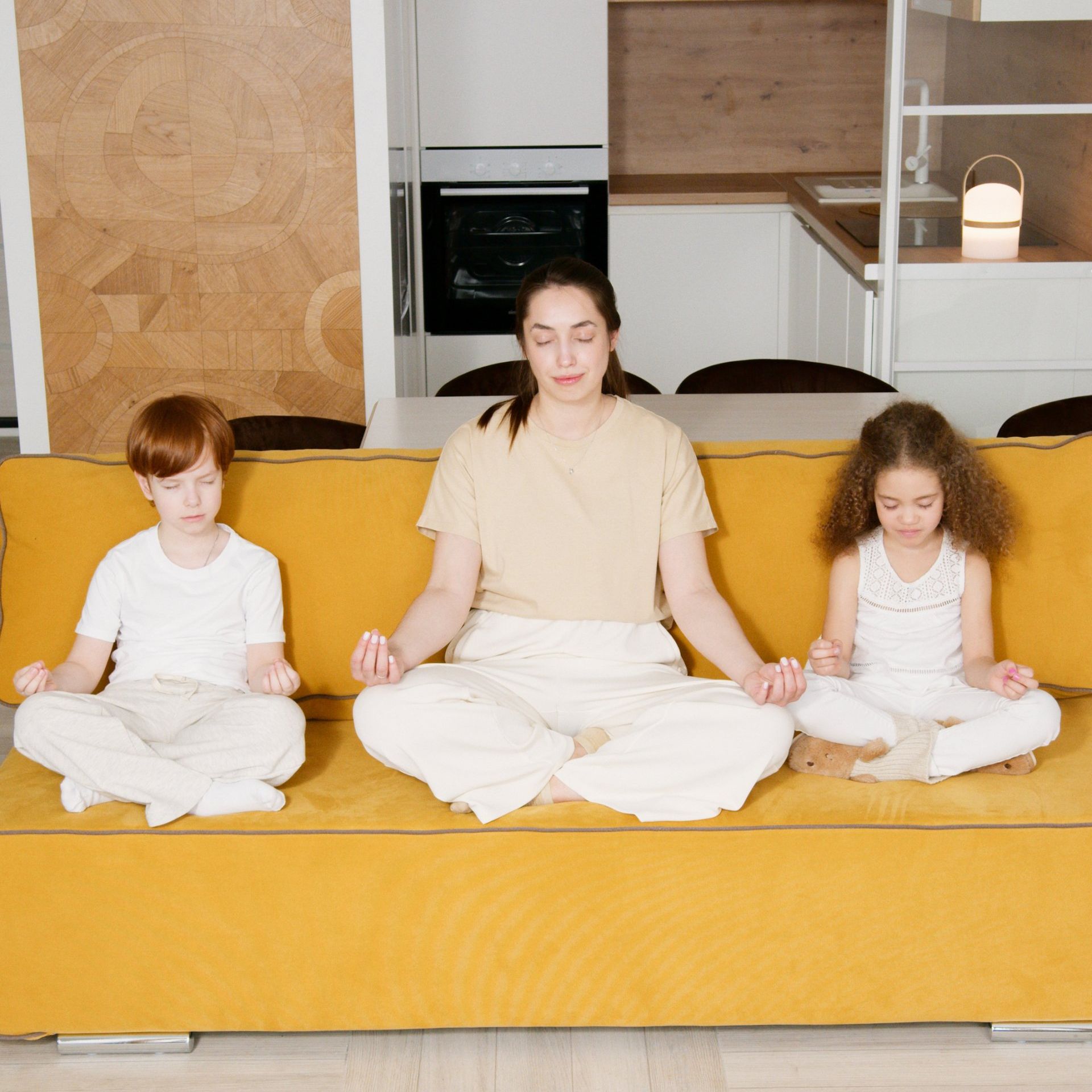 Image of mother and children meditating on their living room sofa.