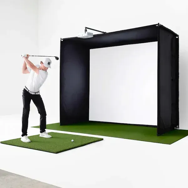 A man is swinging a golf club in front of a large screen.