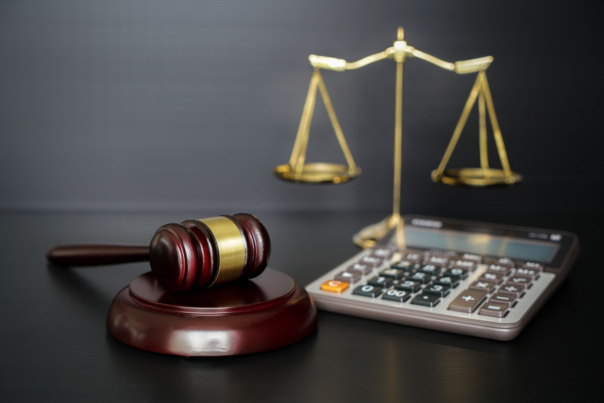 A judge 's gavel , scales of justice and a calculator on a table.