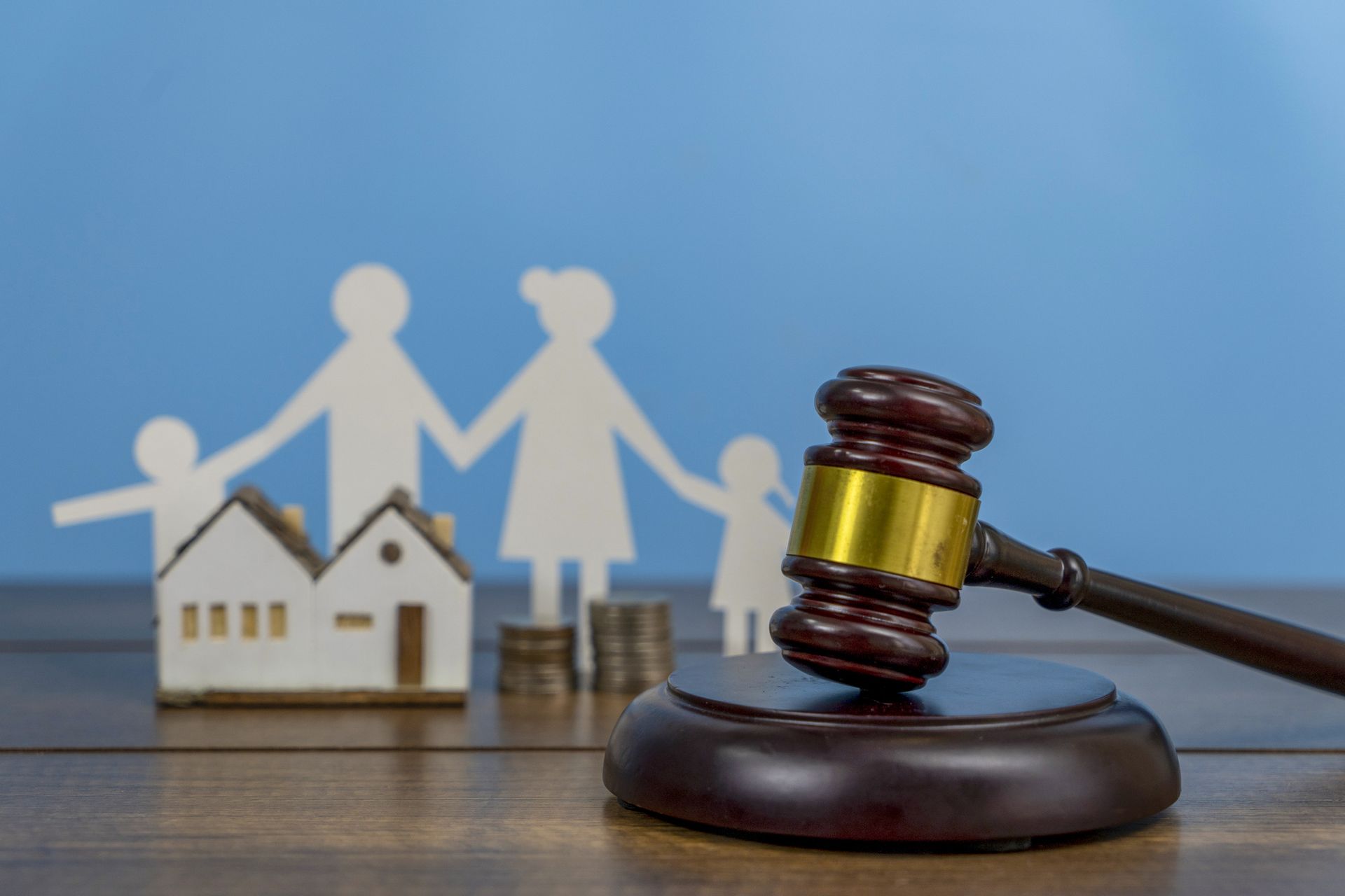 A wooden gavel is sitting on a wooden table in front of a paper cut out of a family and a house.