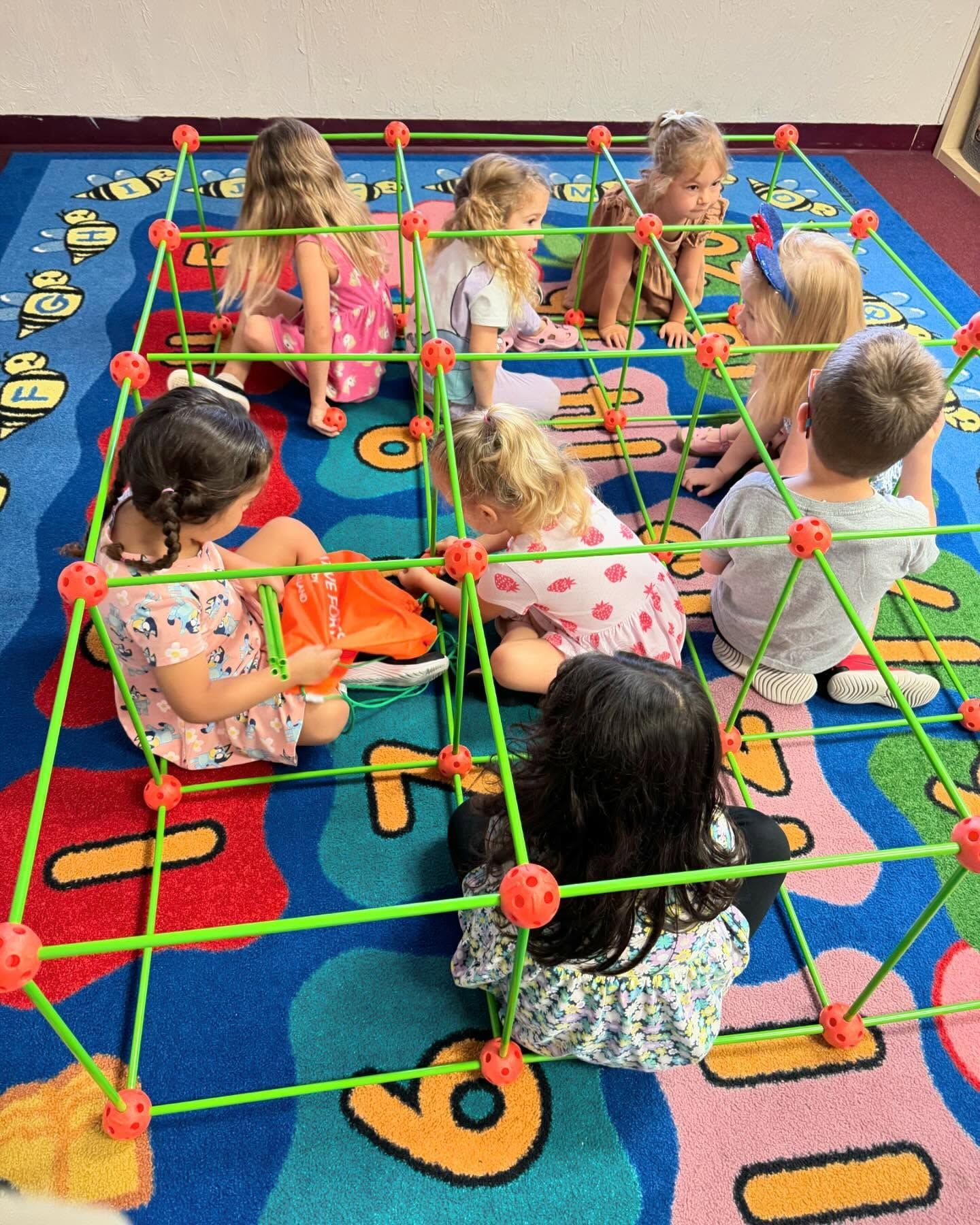 Children playing inside a green and orange geometric structure on a colorful rug.