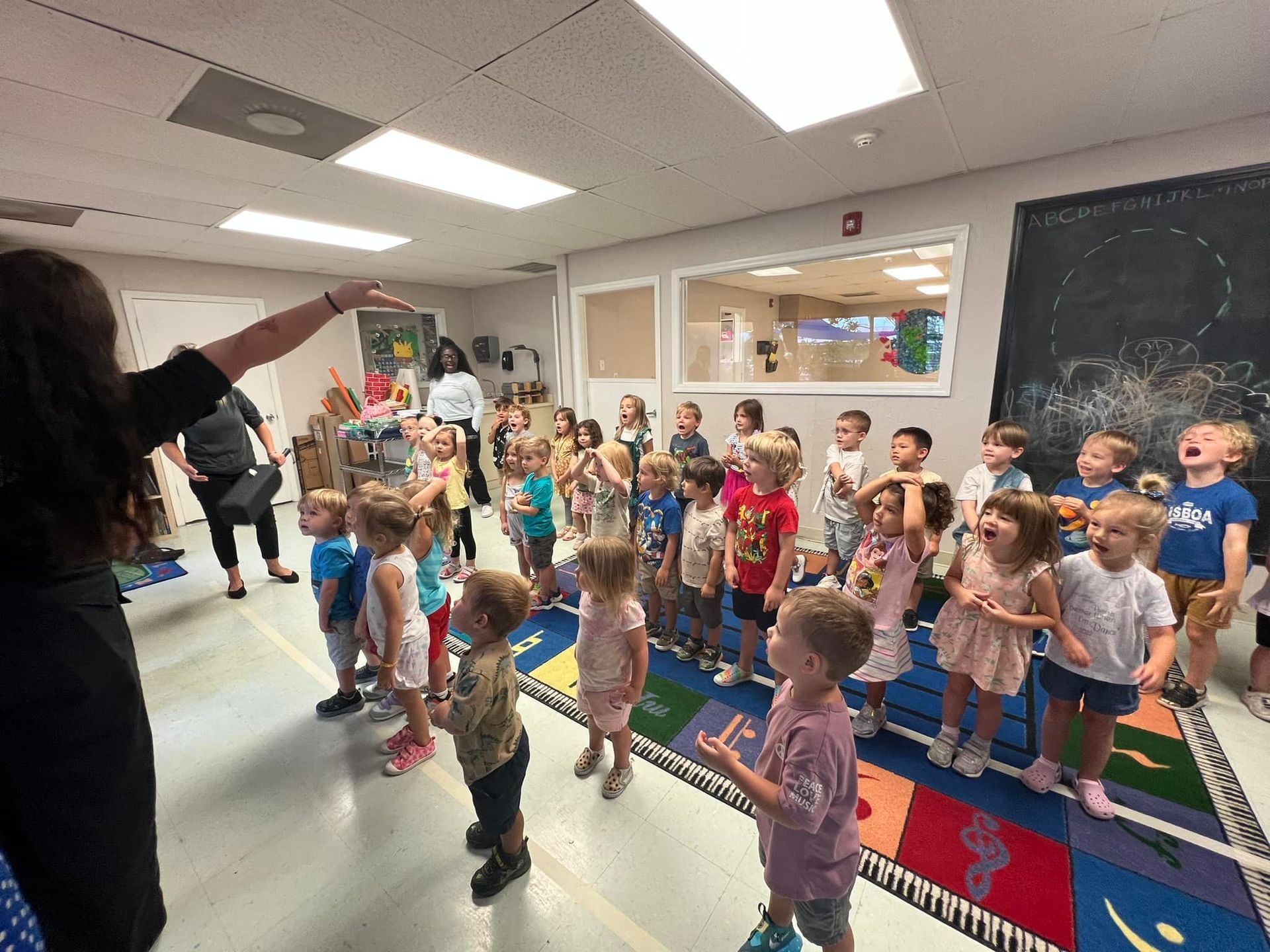 Children in a classroom look up, teacher points. Interior shot.