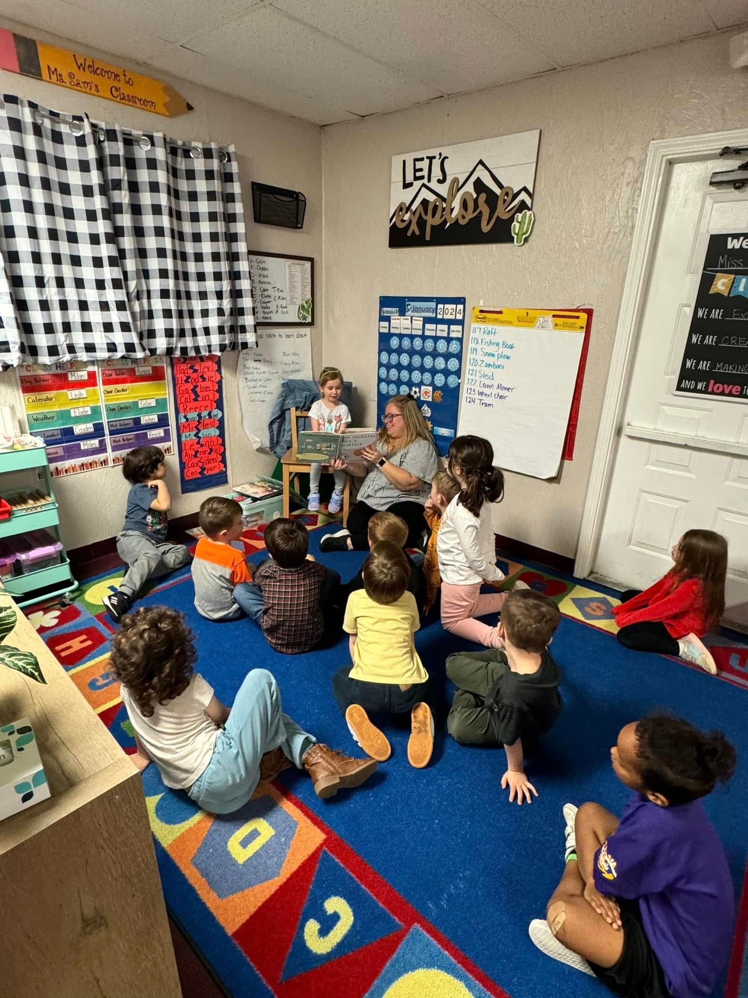 Children and teacher reading in a colorful classroom setting with rug, calendar, and decorations.