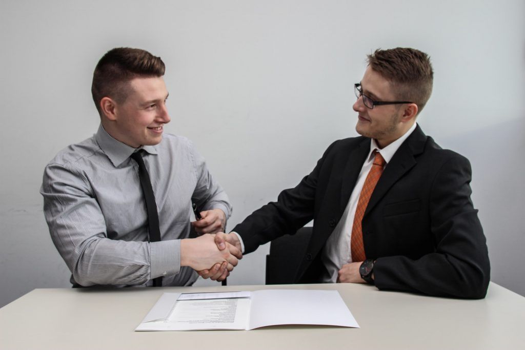 Two men are shaking hands while sitting at a table.