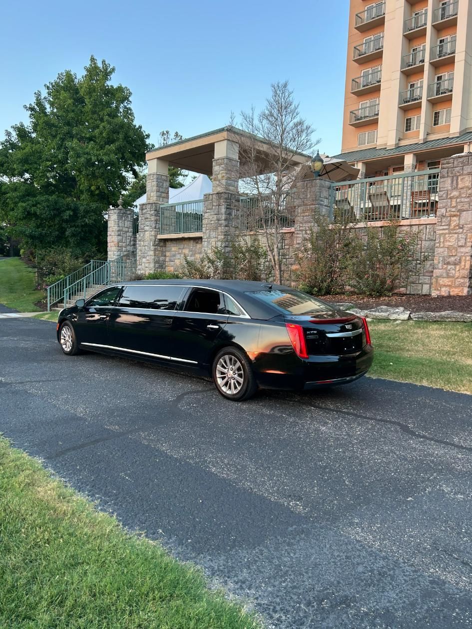 Black sedan parked on a driveway near a stone building and a high-rise hotel.