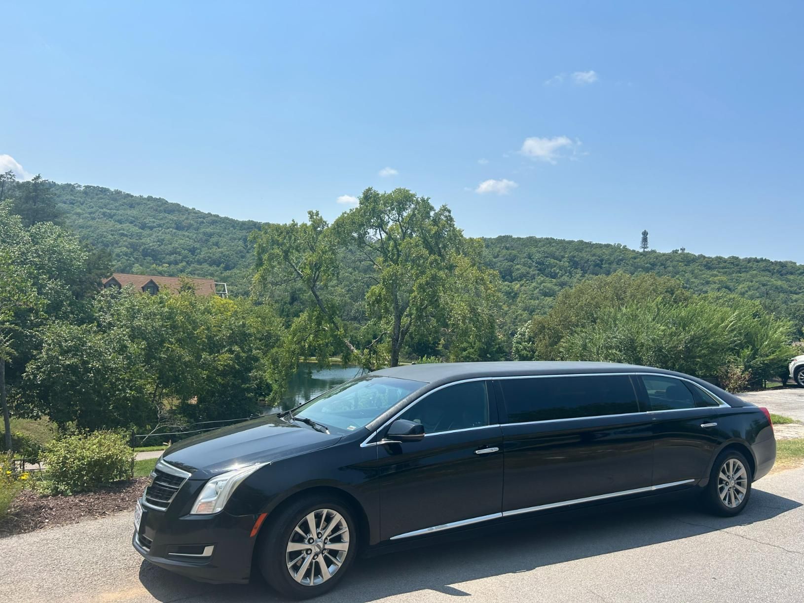 Black limousine parked outdoors with a mountain backdrop, under a blue sky.