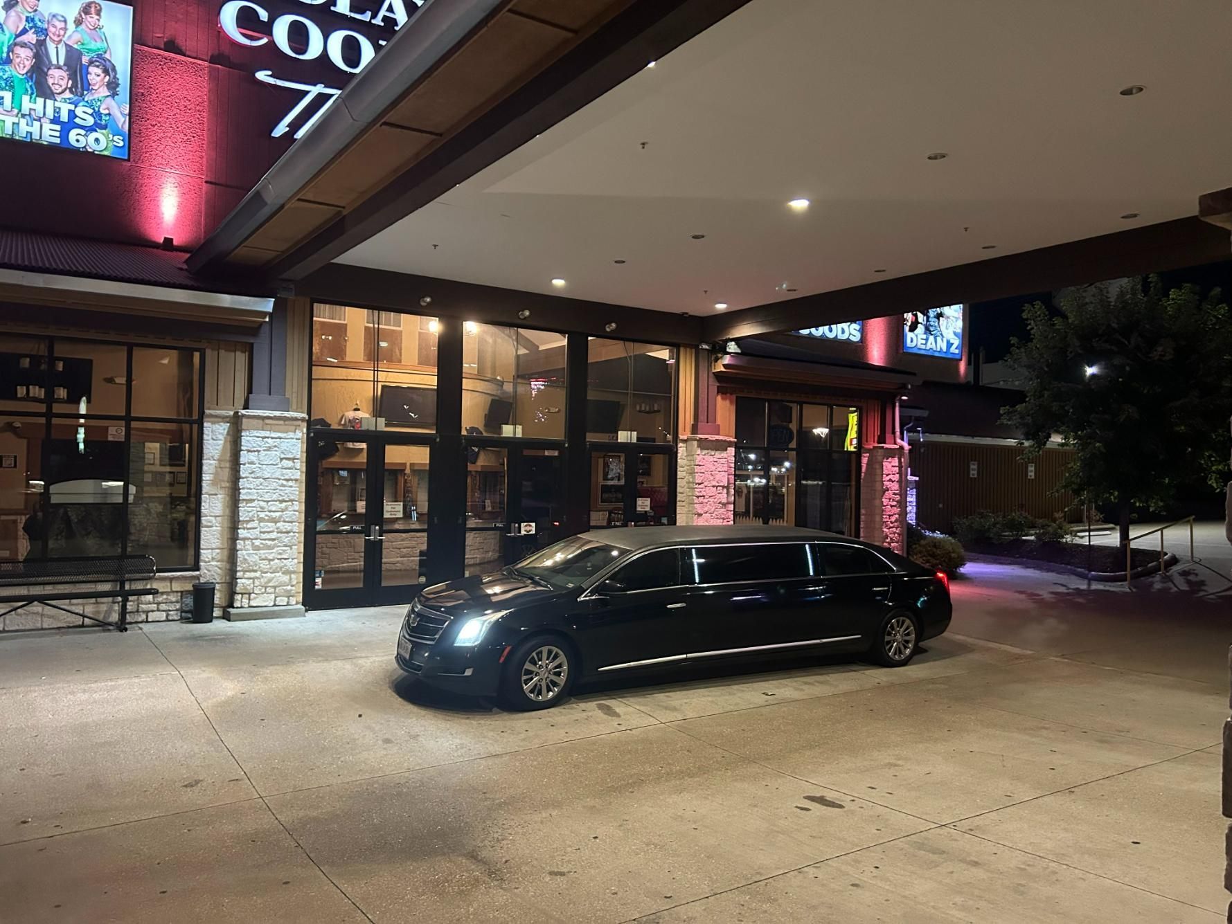 A black limousine parked under the entrance canopy of a building at night.