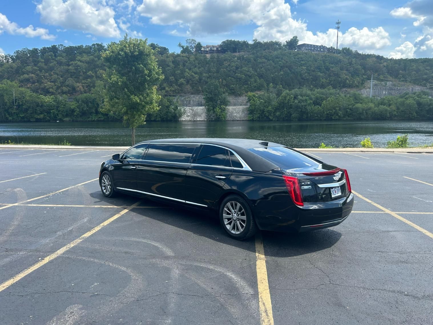 Black limousine parked in a lot with a lake and greenery in the background. Sunny day.