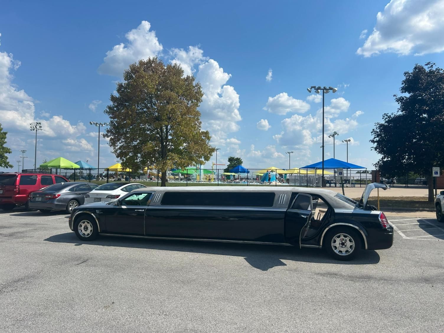 Black limousine parked in a parking lot on a sunny day near a recreational area.