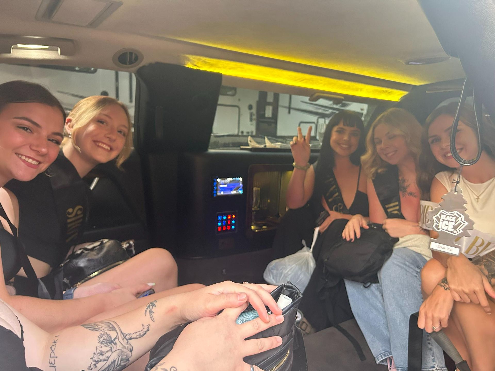 Six women inside a limousine, smiling and posing. One is flashing a peace sign. Interior is black and gold.