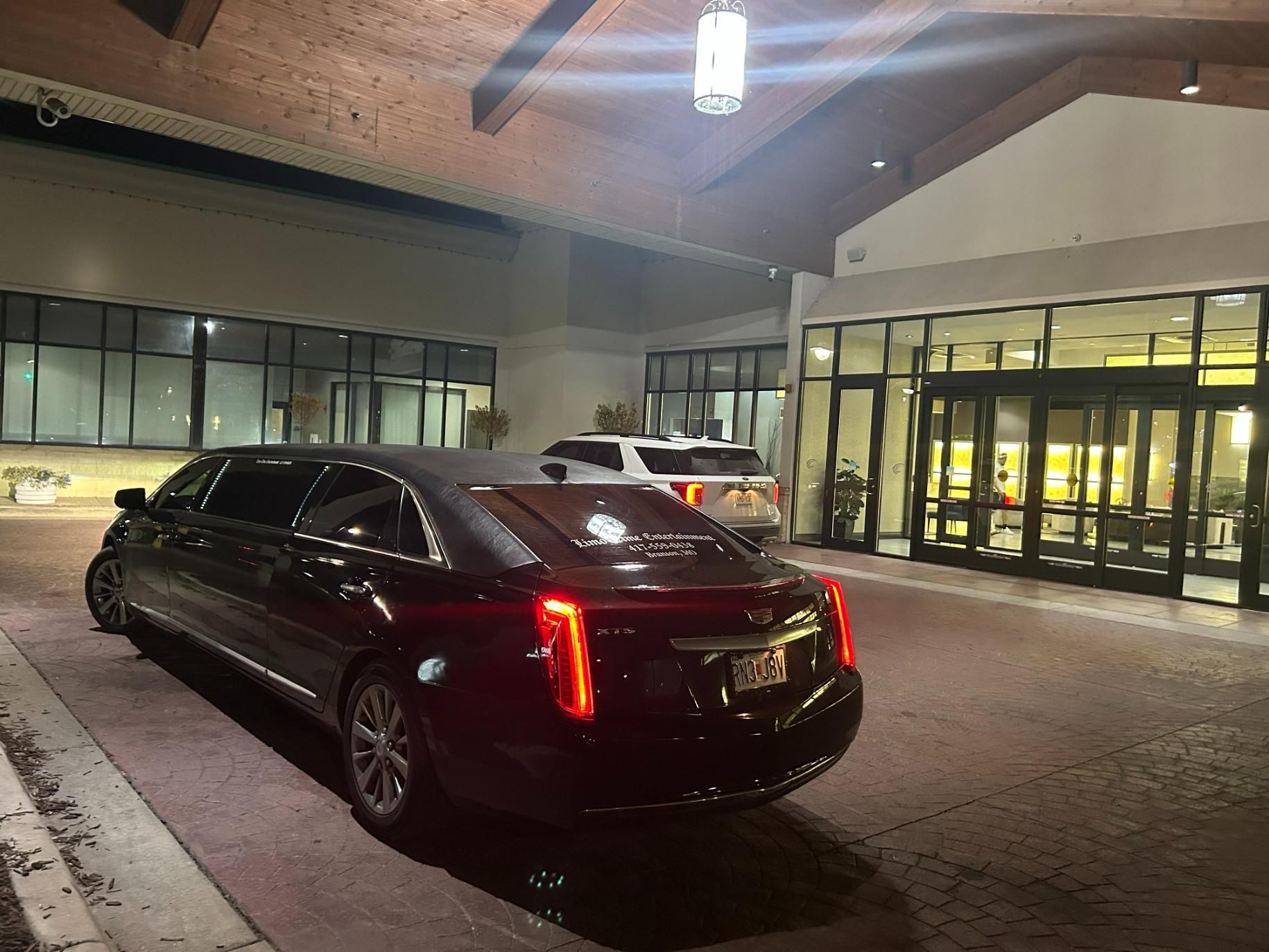 Black limousine parked in front of a building entrance with glass doors and windows.