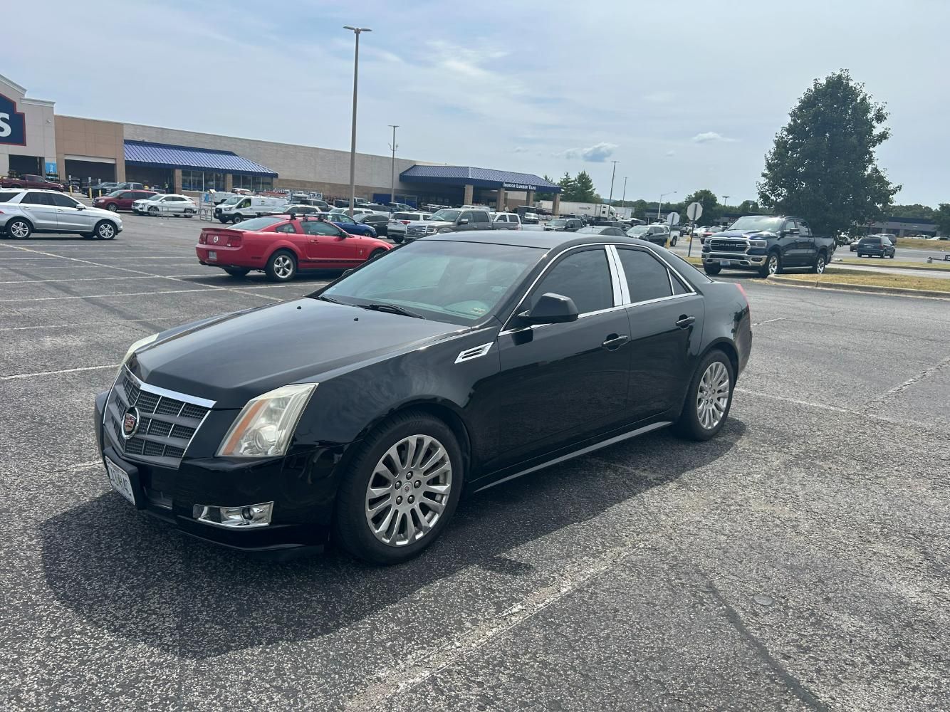 Black Cadillac sedan parked in a lot in front of a Lowe's store on a sunny day.