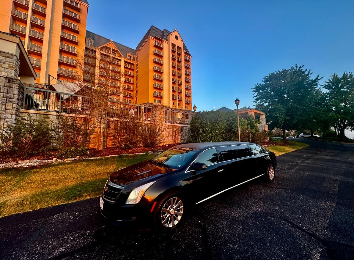 Black limousine parked in front of a tall, orange-tinted building, possibly a hotel, at sunset.