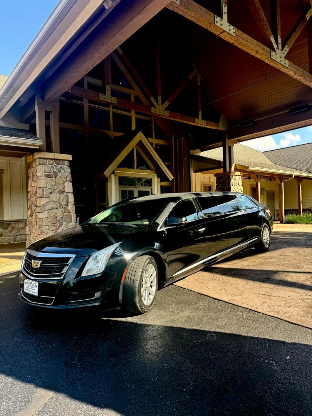 Black limousine parked under a building's entrance canopy. Daytime, sunny.