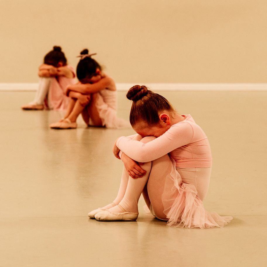 Three young ballerinas are sitting on the floor with their heads down