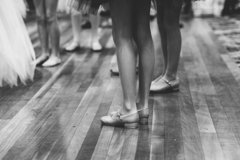 A black and white photo of a group of people standing on a wooden floor.