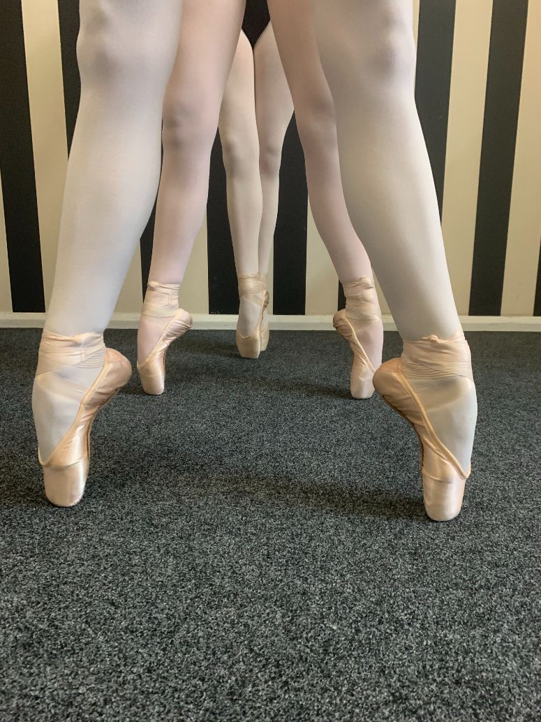 Three ballerinas are standing next to each other wearing pointe shoes.