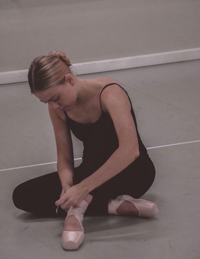A woman is sitting on the floor tying her ballet shoes — Studi-O Dance School In Gateshead, NSW