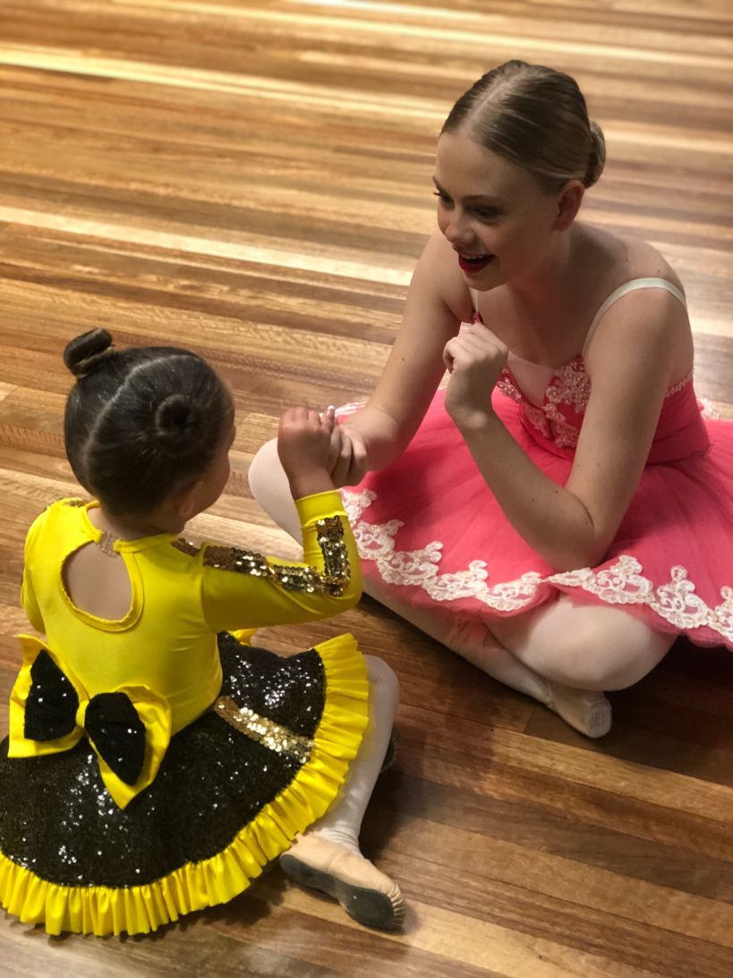 Two Young Ballerinas Are Sitting on the Floor Holding Hands — Studi-O Dance School In Gateshead, NSW