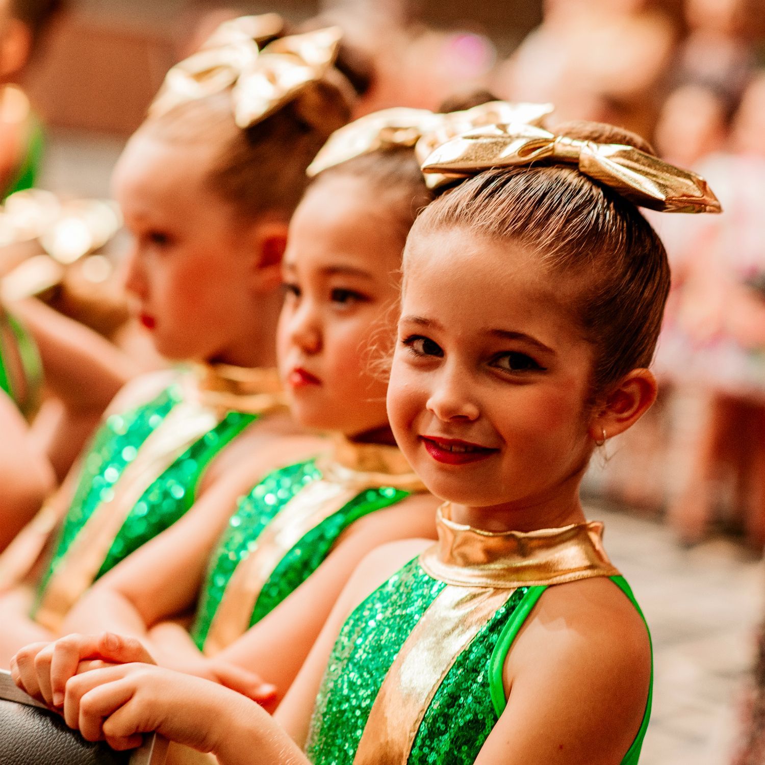 A group of young girls wearing green and gold outfits with bows in their hair
