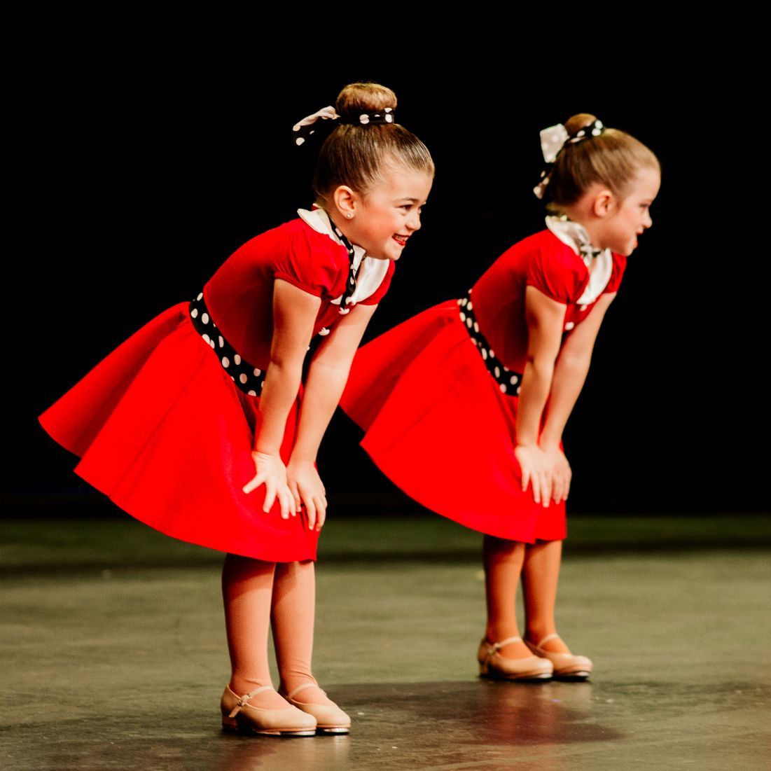 Two Little Girls in Red Dresses Are Standing Next to Each Other on a Stage — Studi-O Dance School In Gateshead, NSW