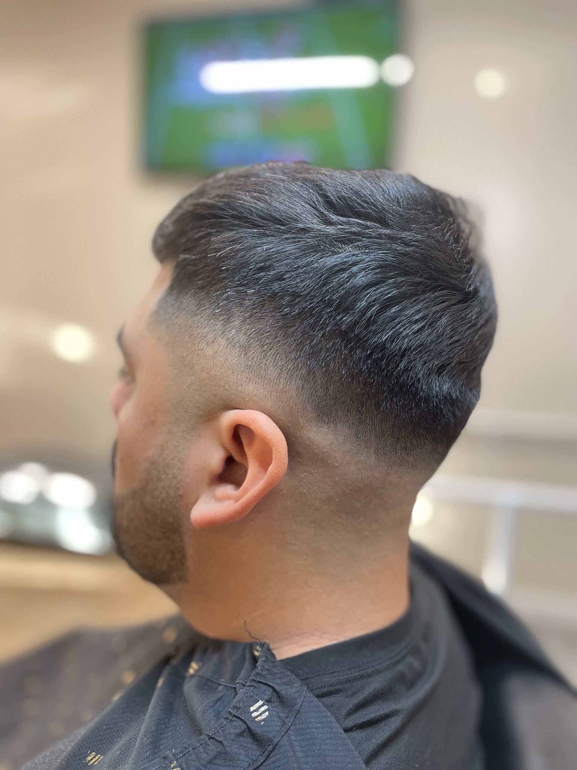 Man with a faded haircut at a salon, dark hair on top, blurred background.