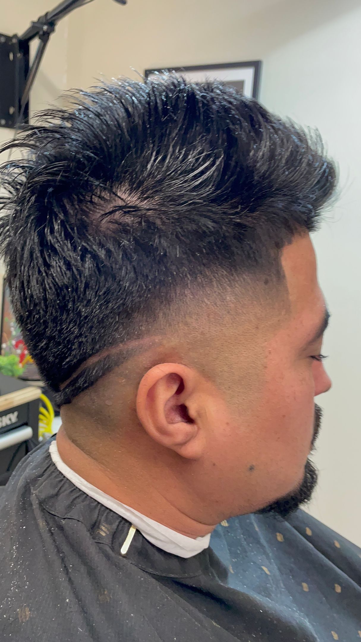 Man with dark hair and a faded haircut, sitting in a barber chair.