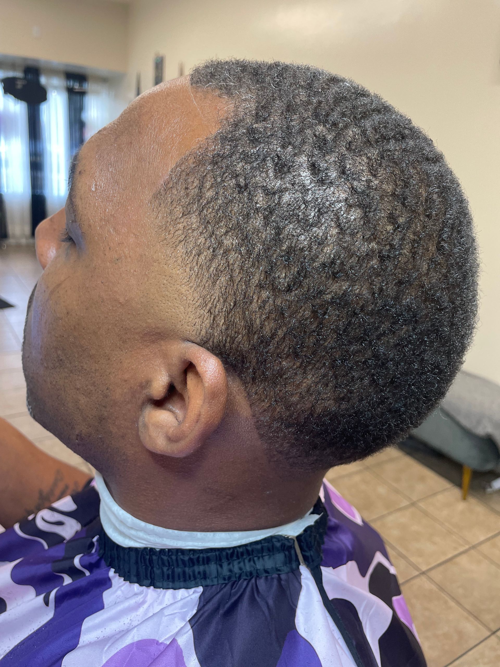 Man with a short, textured haircut, wearing a purple and white barber's cape; in a salon.