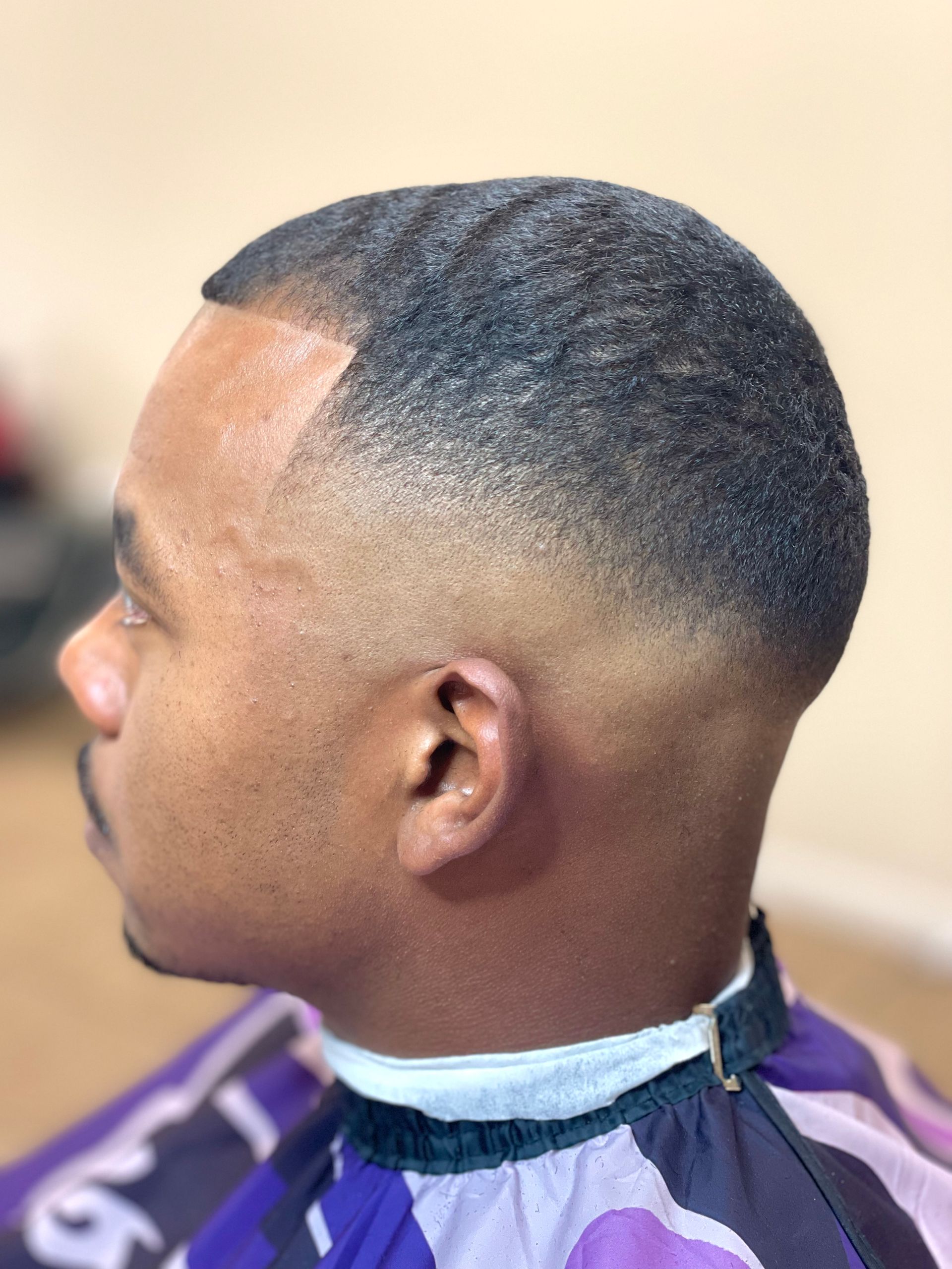 Man with faded haircut, skin-toned, with dark hair on top. Wearing a purple and black cape.