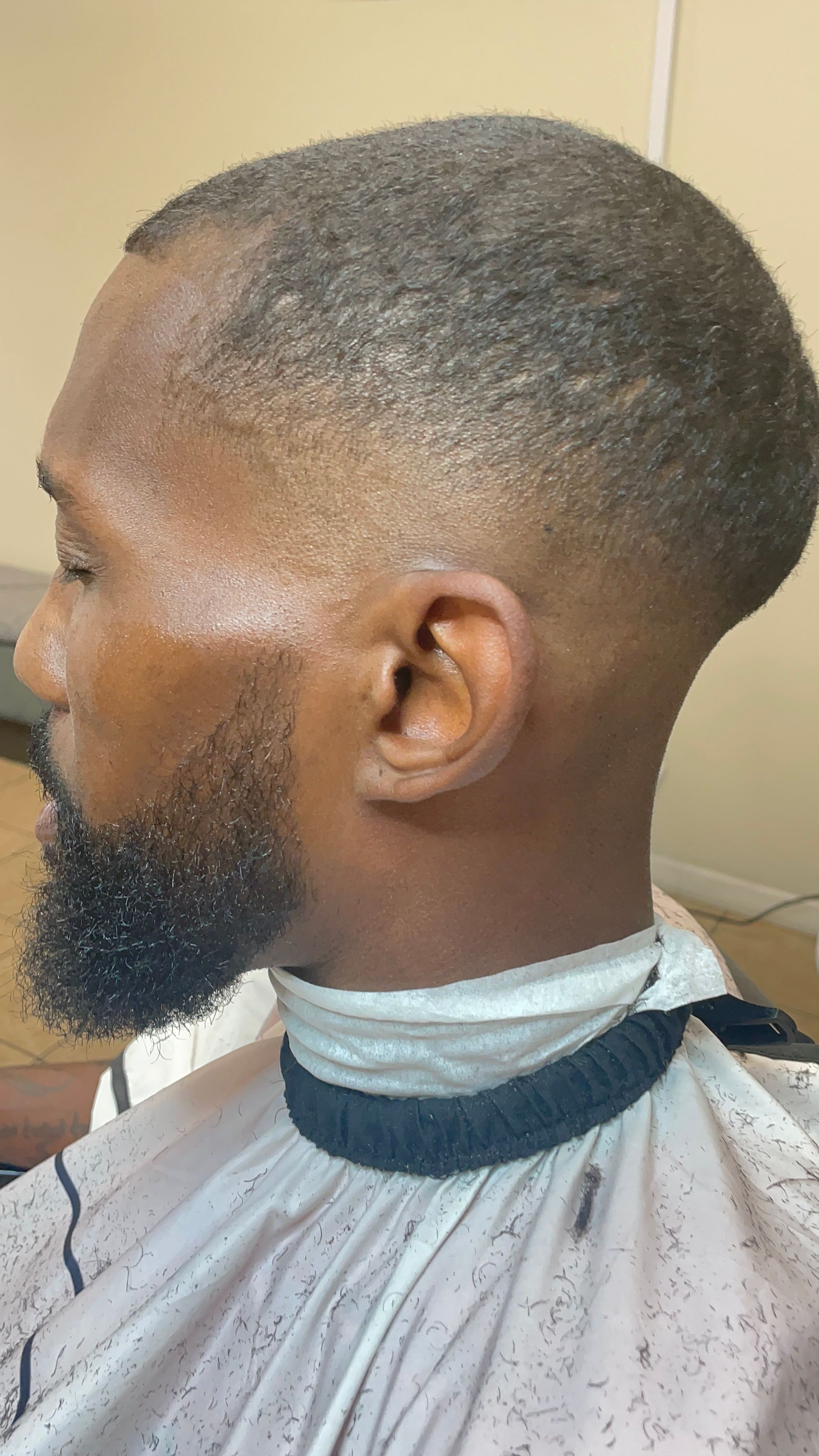 Man with faded haircut and beard; wearing a barber cape.