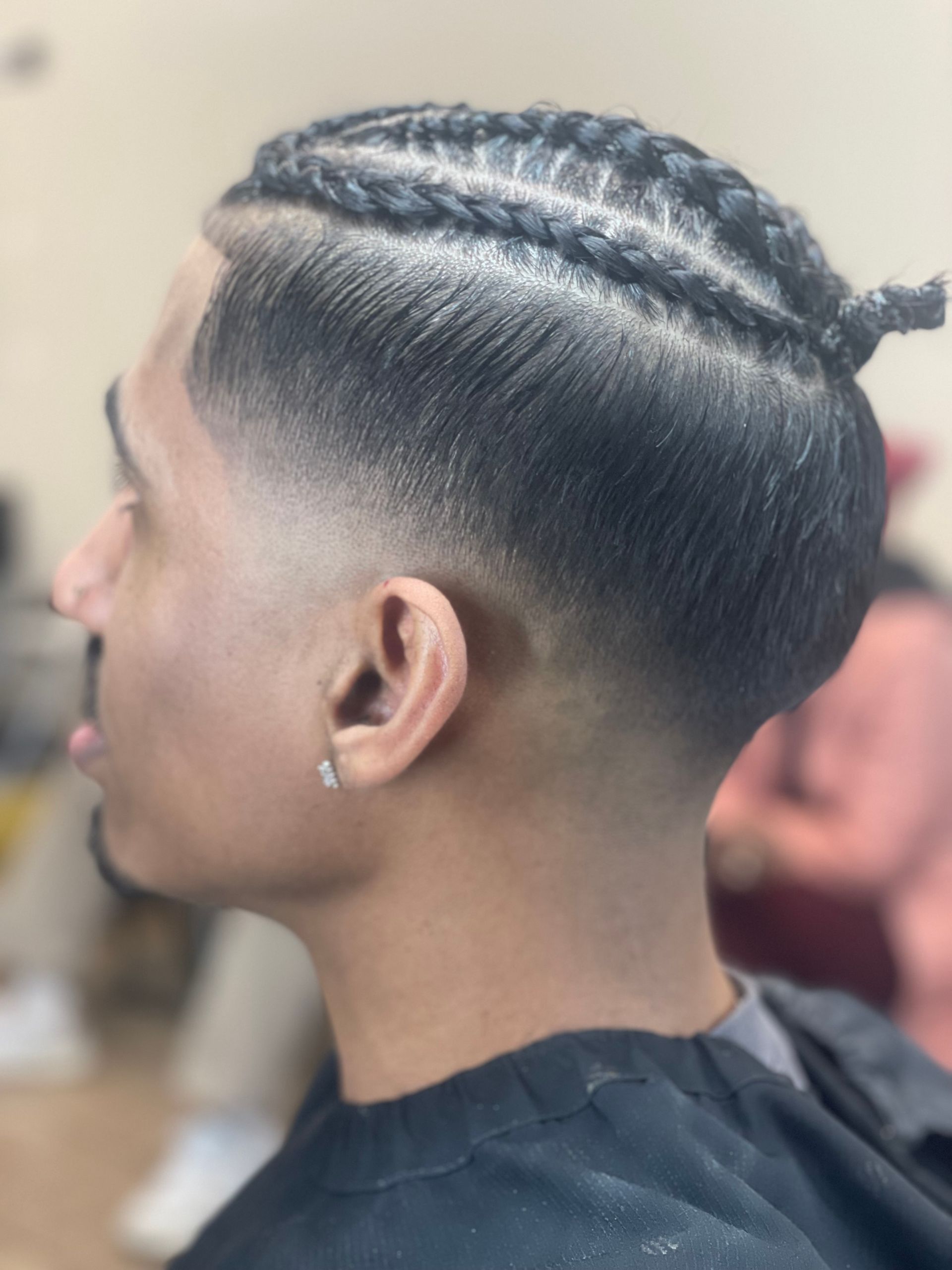 Man with braided hairstyle and faded sides, ear with earring.
