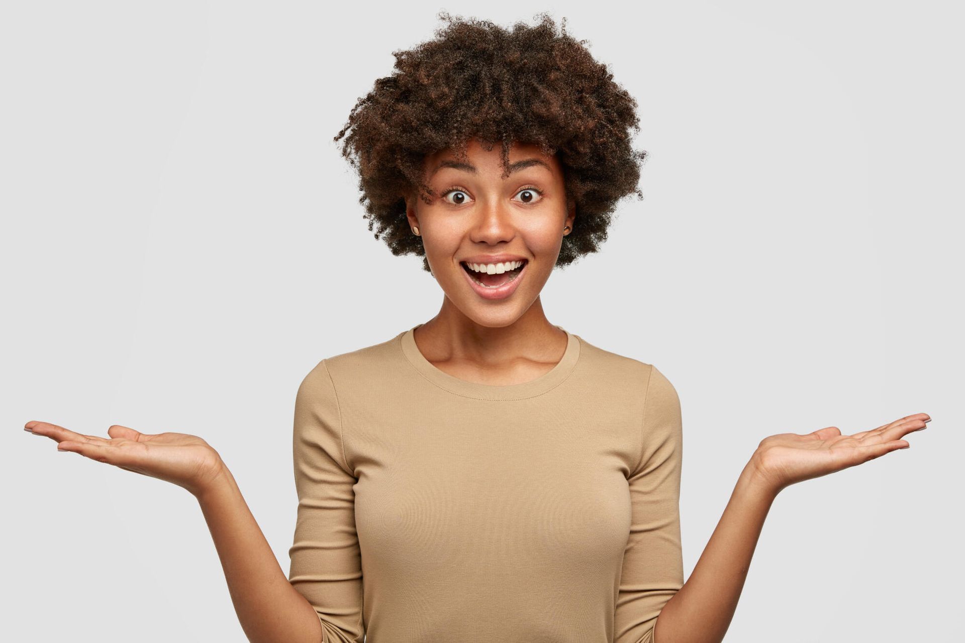 Young woman with brown skin and curly hair, smiling widely, palms up.