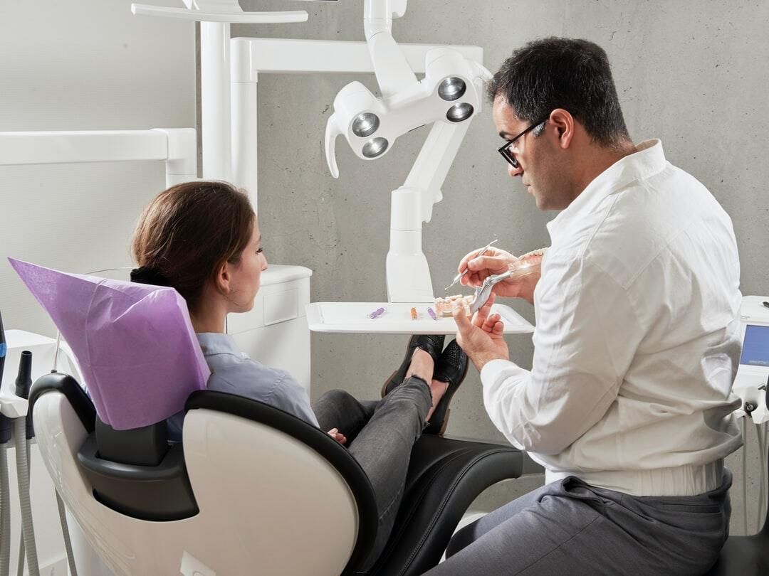 Dentist showing model teeth to a patient in a dental chair. The patient is looking at the dentist.