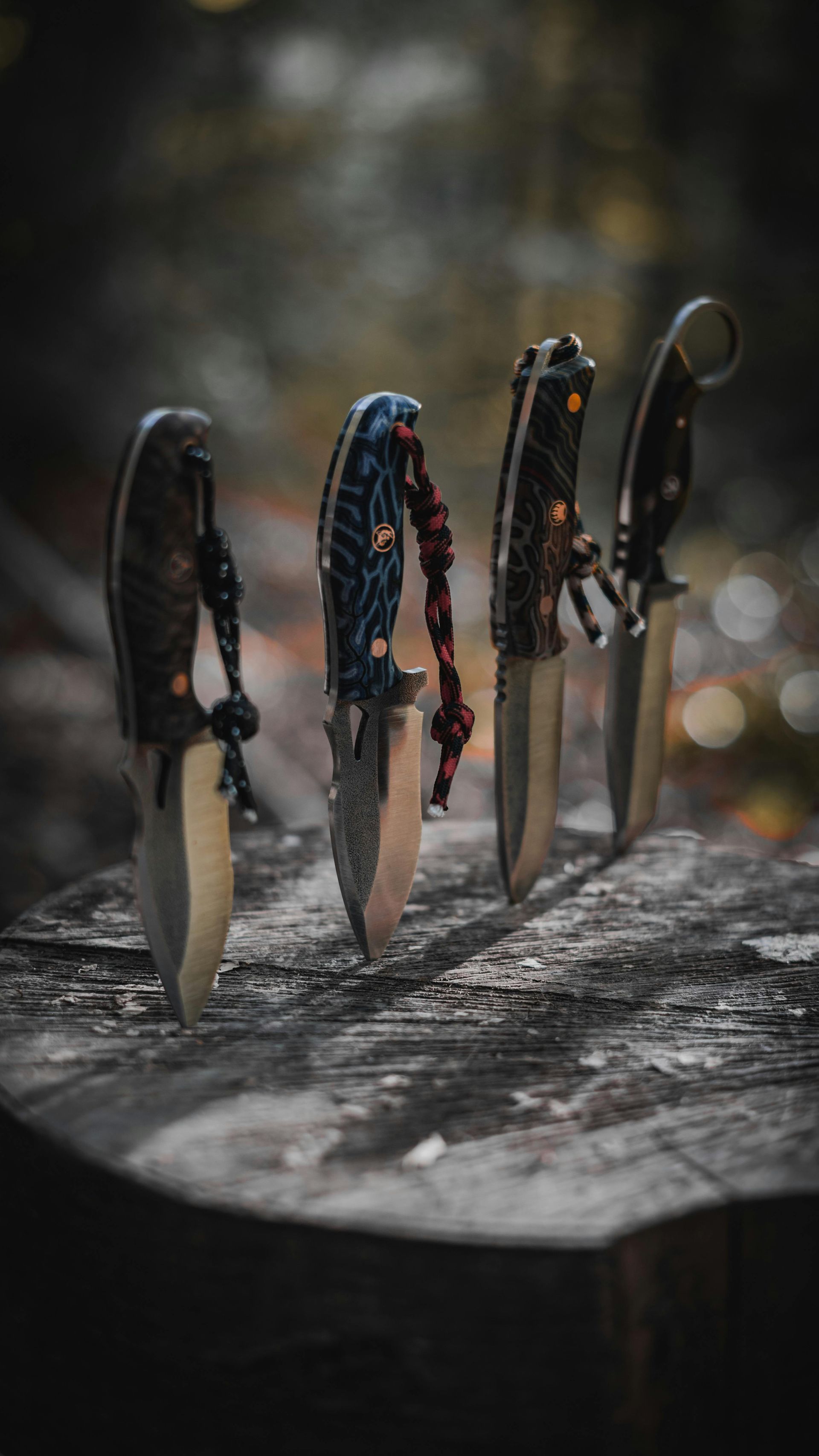 Four knives with decorative handles standing upright in a rough wooden surface.