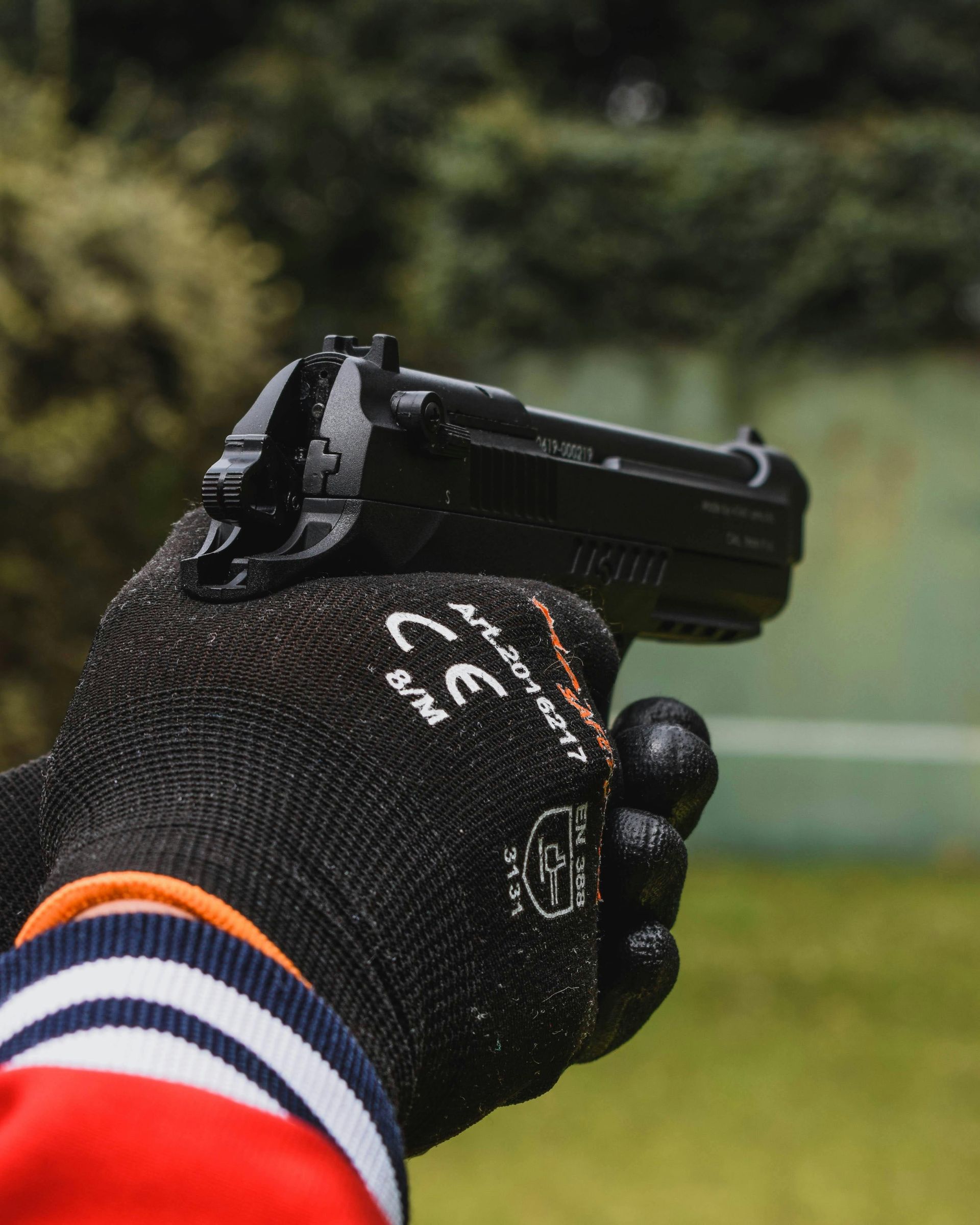 Person in black glove holding a black handgun, against a green grassy background.