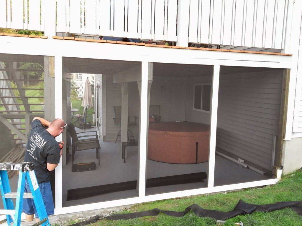 A man is standing on a ladder in front of a screened in porch.