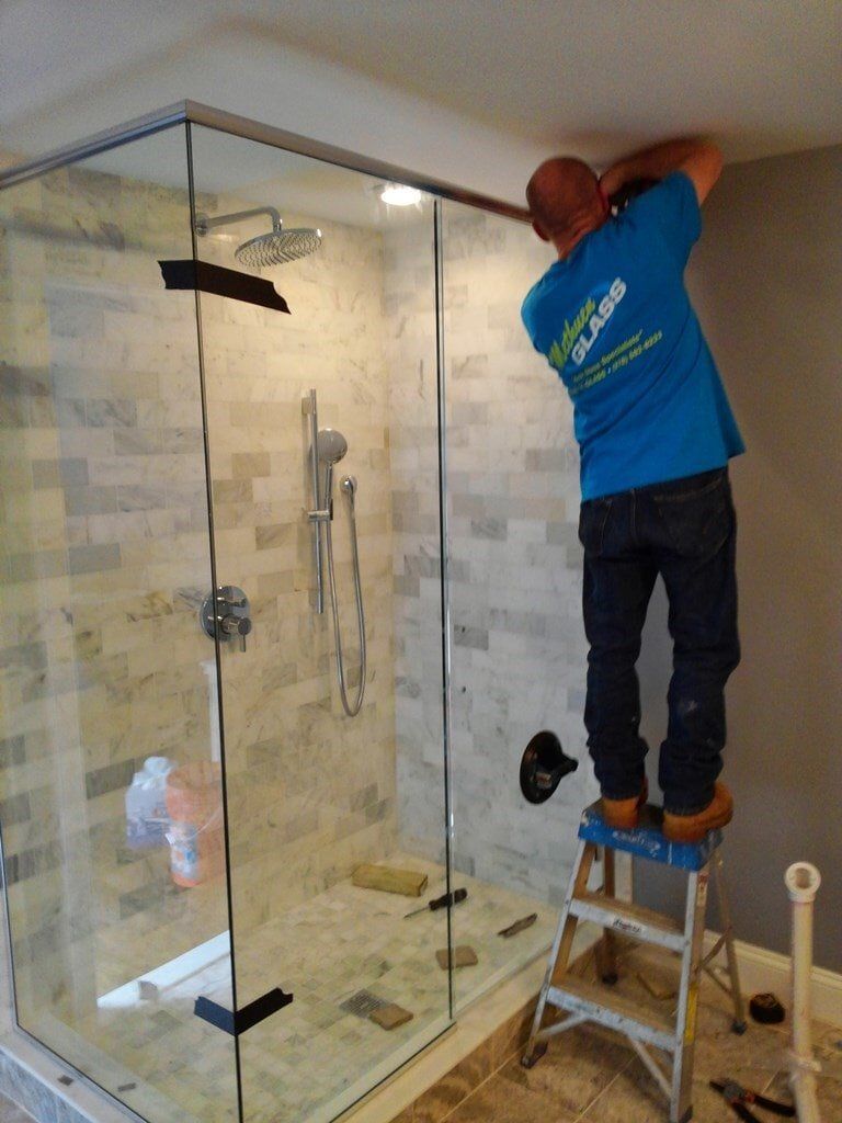 A man in a blue shirt is standing on a ladder in front of a shower stall.