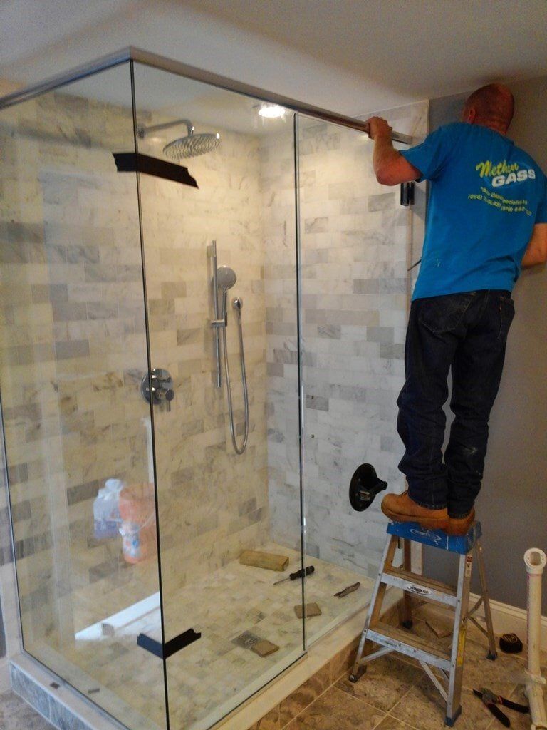 A man is standing on a ladder in front of a shower stall.