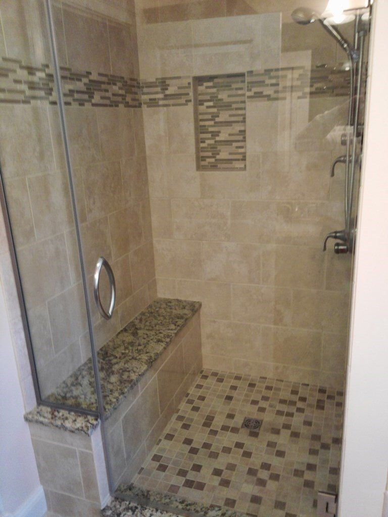 A walk in shower with a glass door and a bench.