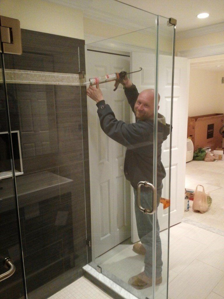 A man is installing a glass shower door in a bathroom.